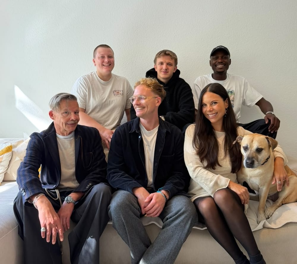 Das Team von Vertraut auf einem Sofa: sechs Menschen und Hündin Nala, alle lachen in die Kamera