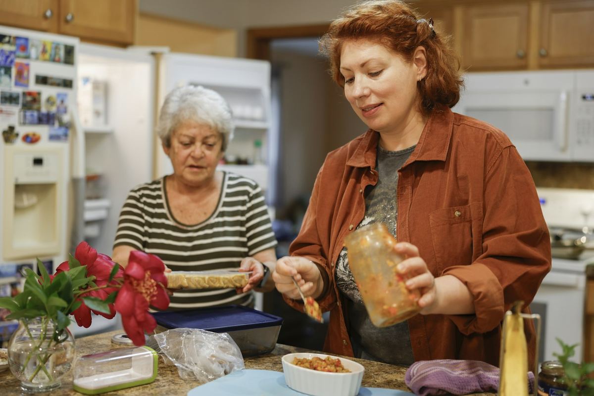 Eine ältere Frau und eine Frau mittleren Alters kochen gemeinsam in einer Küche.