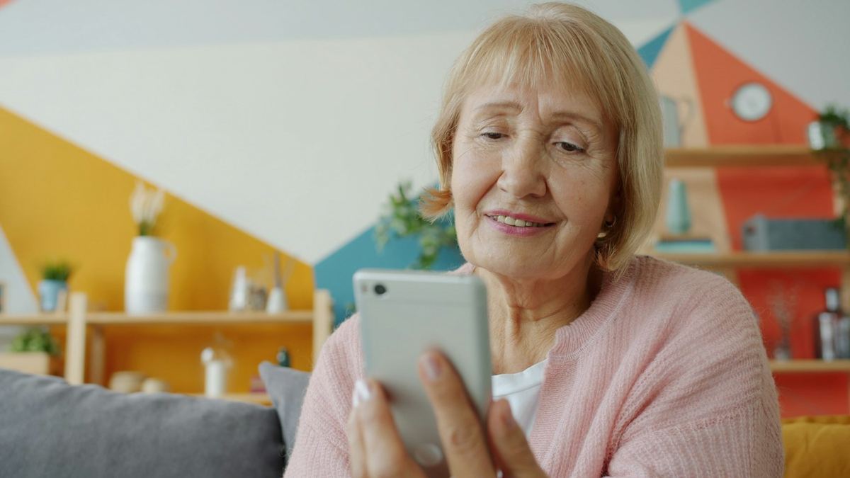 Eine ältere Frau hält ein Smartphone in der Hand und lächelt in einen Videoanruf.